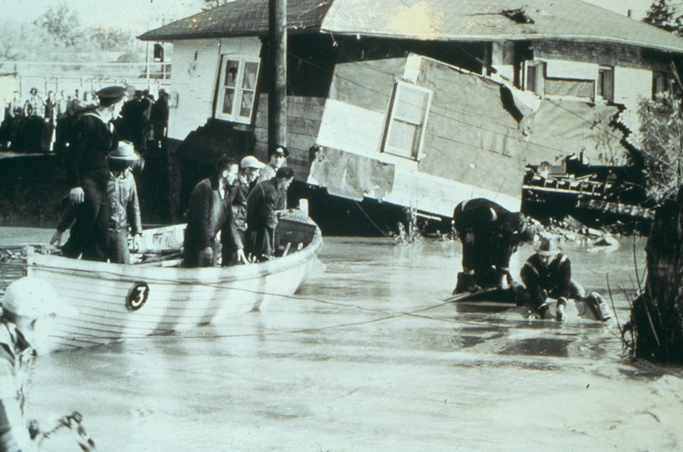 People on a boat over flooded streets while a damaged house is visible at the background after Hurricane Hazel impacted the City of Toronto in the 1950s