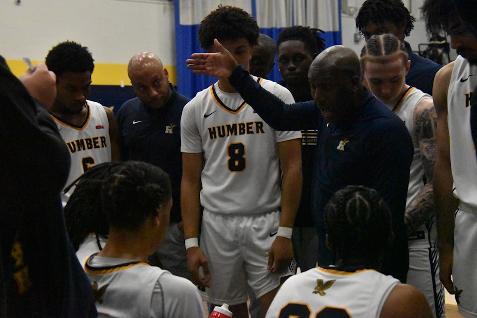 Man in blue sweater talks to Humber Hawks players during a timeout